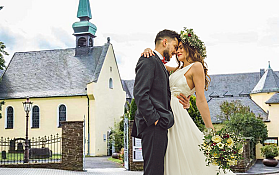 Ein Brautpaar umarmt sich vor einer Kirche im Freien.
