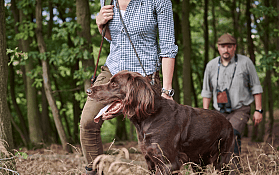 Ein älterer Mann mit einem Hund und einem Gewehr in der Natur.