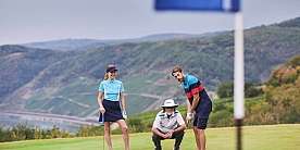 Drei Golfer auf dem Platz, einer puttet, zwei beobachten.