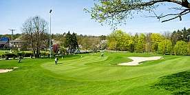 Grüner Golfplatz mit Spielern und Bunkern unter blauem Himmel.
