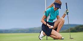 Eine Golferin kniet und hält einen Golfball auf dem Grün.