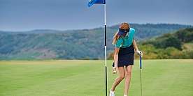 Eine Golfspielerin hebt den Ball am Loch auf.