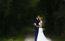 Ein Brautpaar küsst sich auf einem Waldweg.