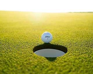 Ein Golfball steht vor einem Golfloch auf grünem Rasen.