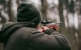 Eine Person zielt mit einem Gewehr in einem Waldgebiet.