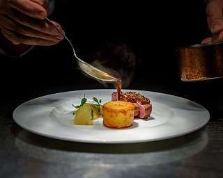 Ein Koch serviert ein kunstvoll angerichtetes Gericht auf einem weißen Teller.